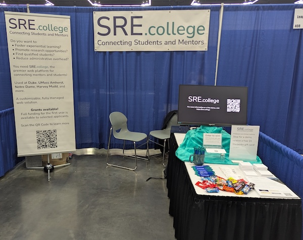 Photo of the SRE.college booth at SICB 2026 with a SRE.collge banner, a vertical sign, and a table with collateral.